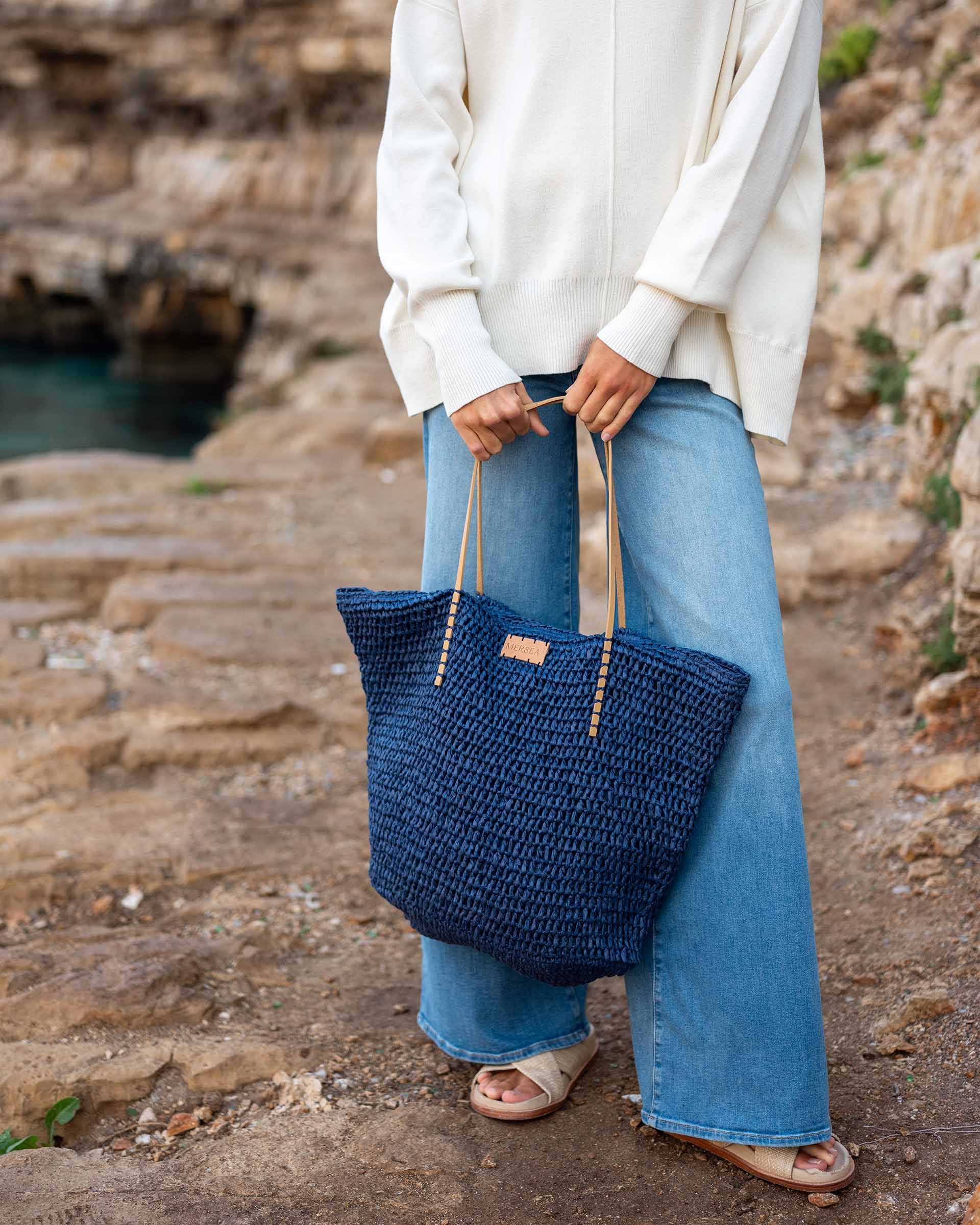 woman holding sun chaser straw tote in navy with jeans on