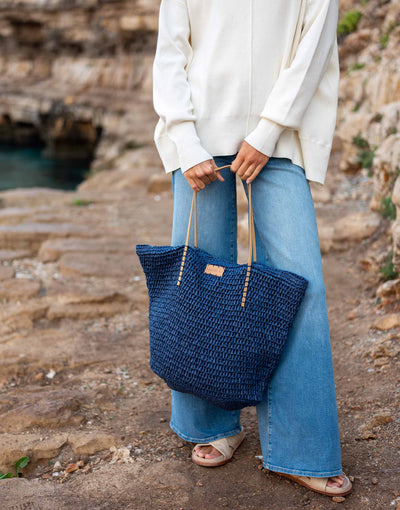 woman holding sun chaser straw tote in navy with jeans on
