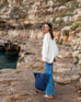 woman on a rock ledge holding sun chaser straw tote in navy