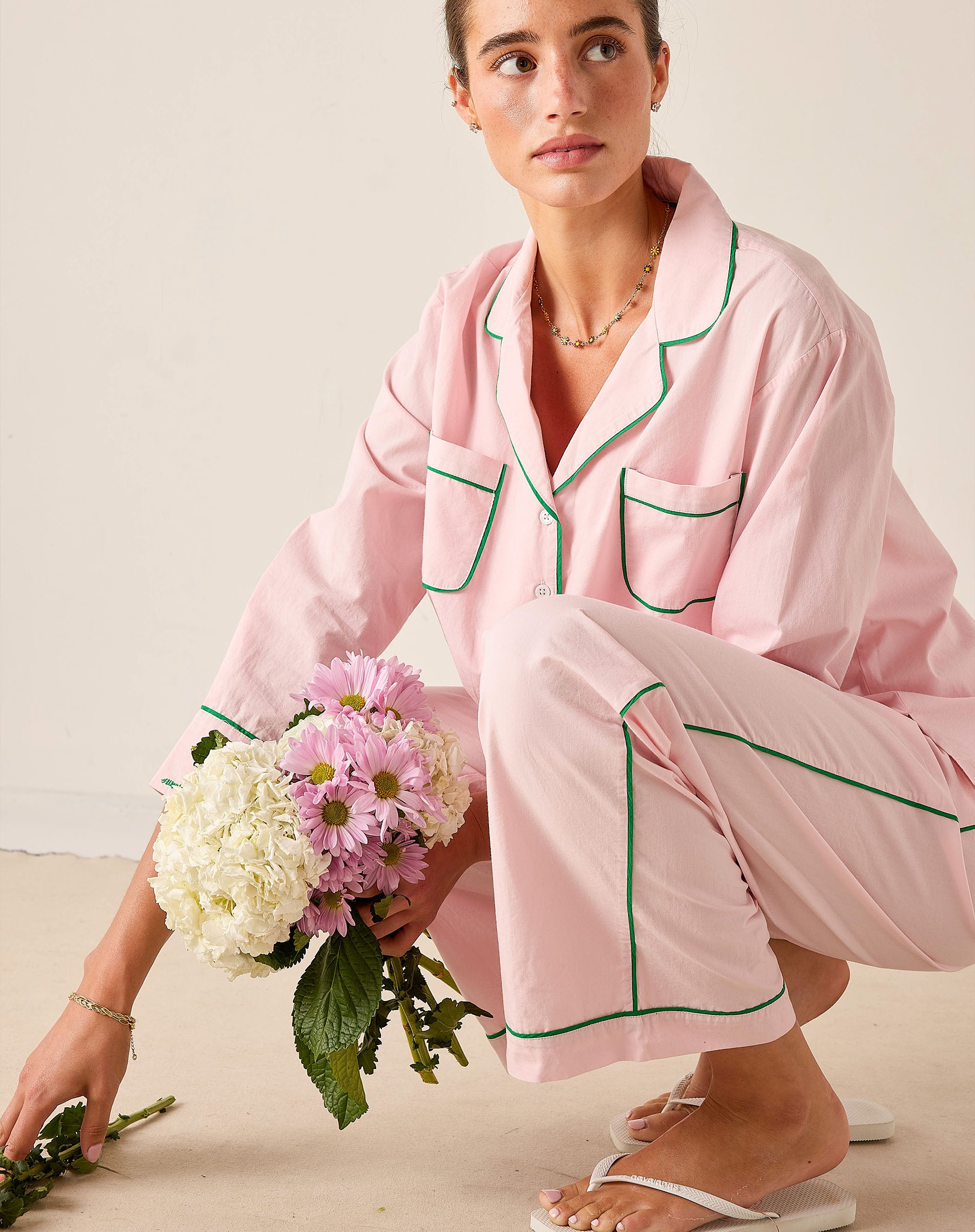 Woman in pink pajama set holding a bouquet of flowers on a neutral background