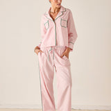 Woman wearing a pink pajama set with black piping against a white background