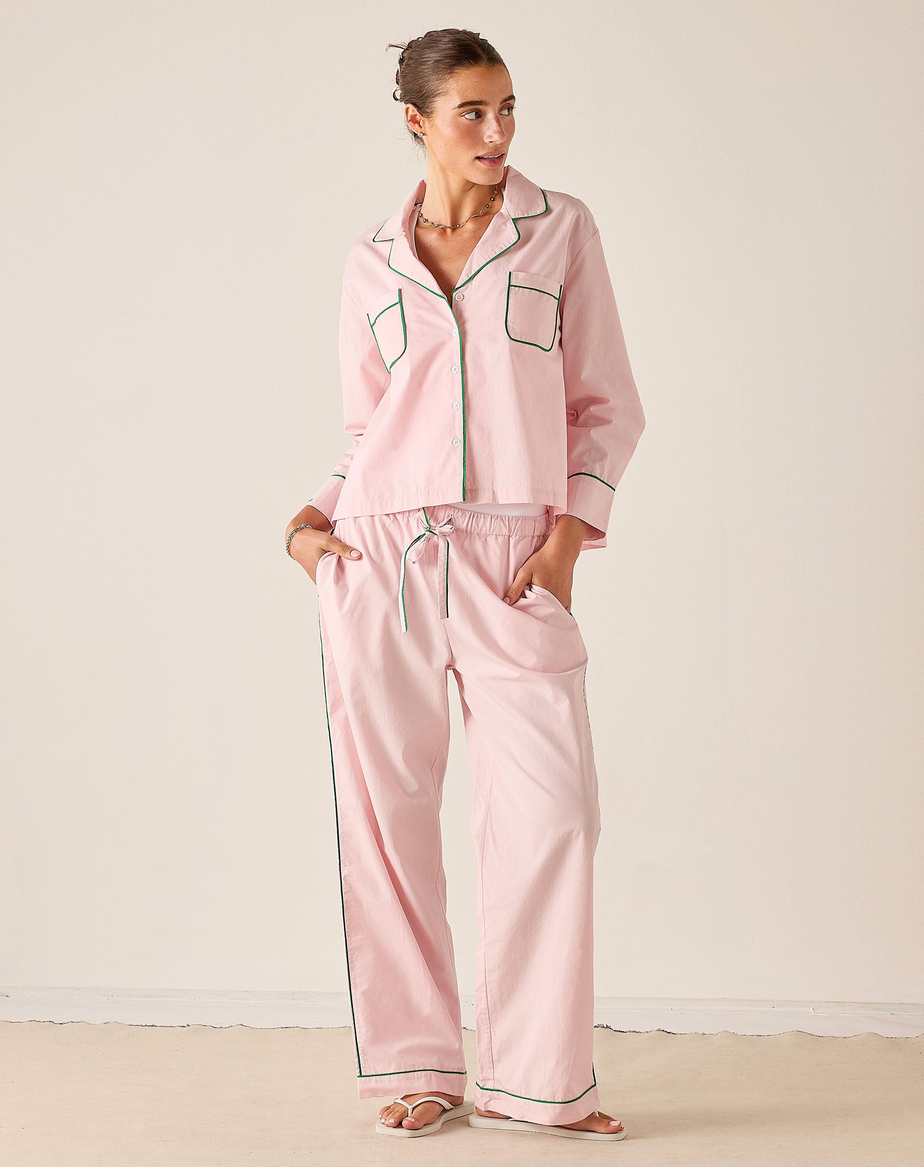 Woman wearing a pink pajama set with black piping against a white background