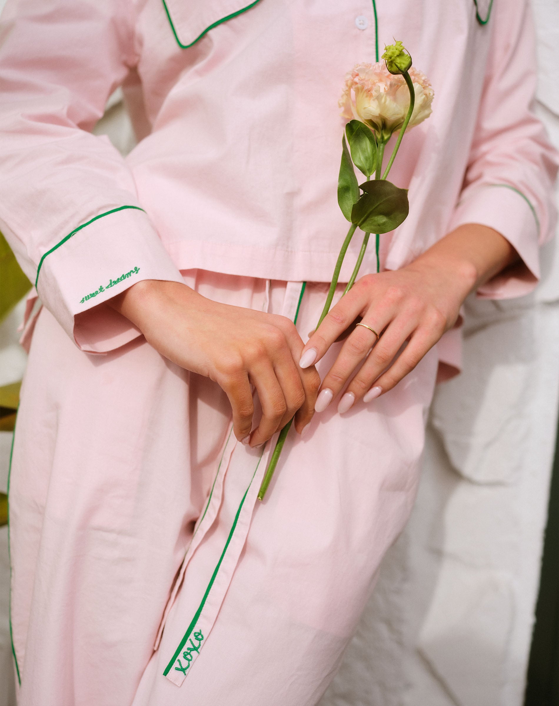 Person wearing a pink outfit with green trim holding a flower.