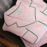 Folded pink shirt with green piping on a wooden surface