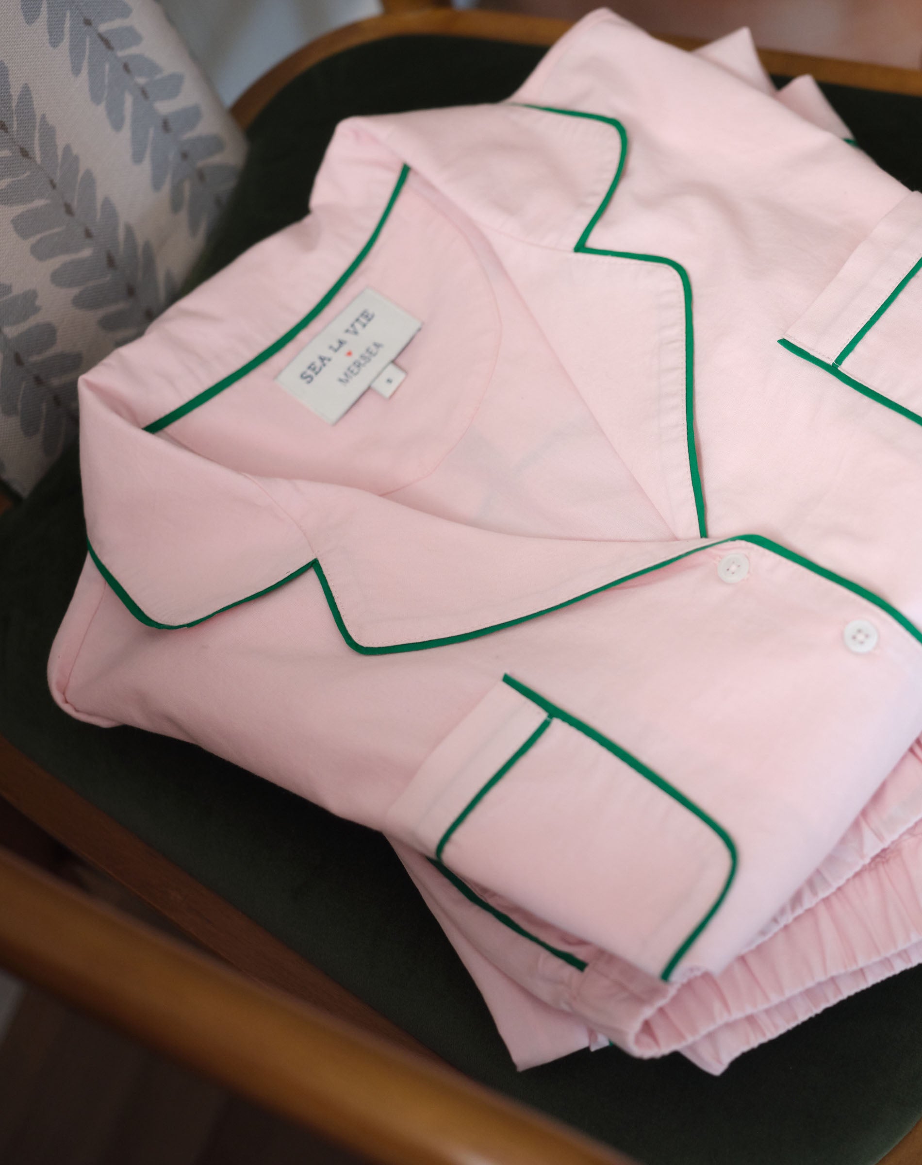 Folded pink shirt with green piping on a wooden surface