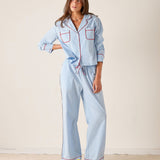 Woman wearing a light blue pajama set with red piping on a plain background
