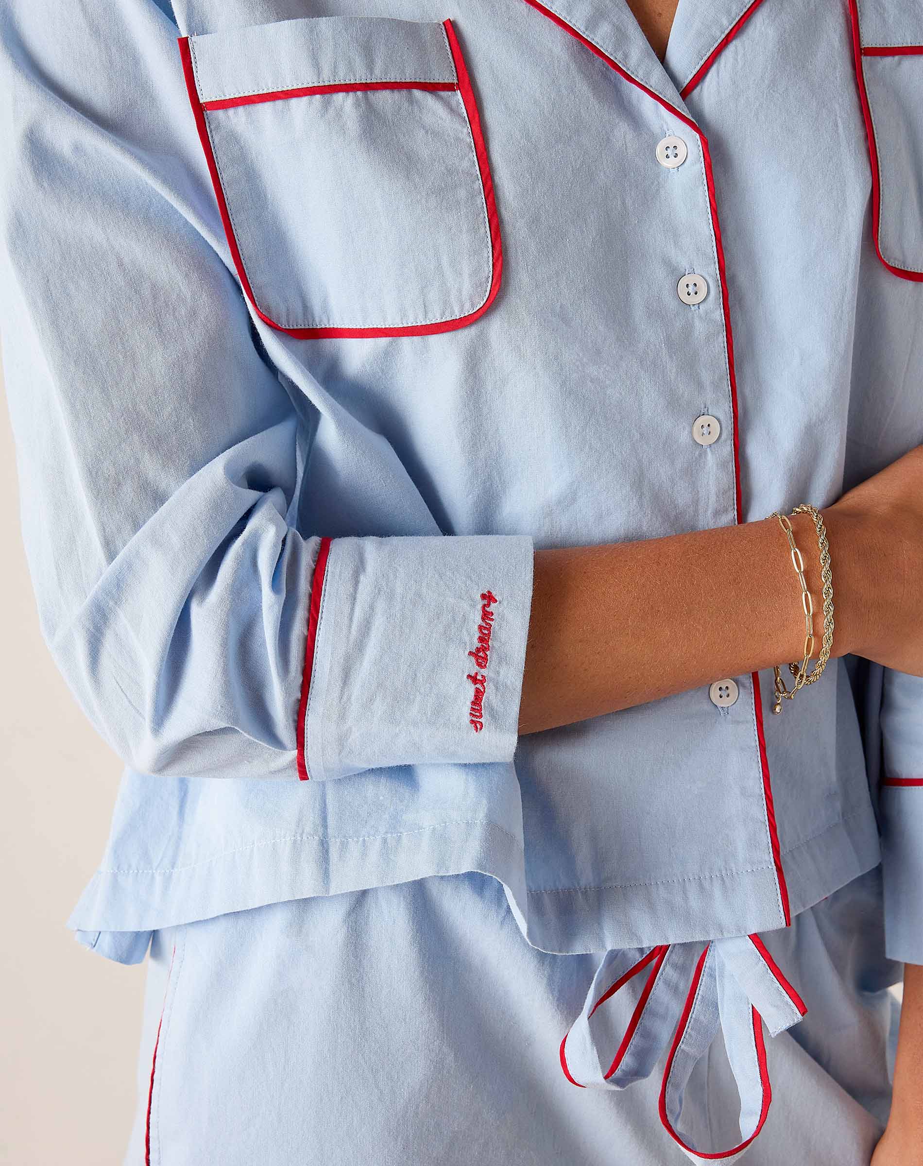 Light blue pajama set with red piping worn by a person, on a neutral background.