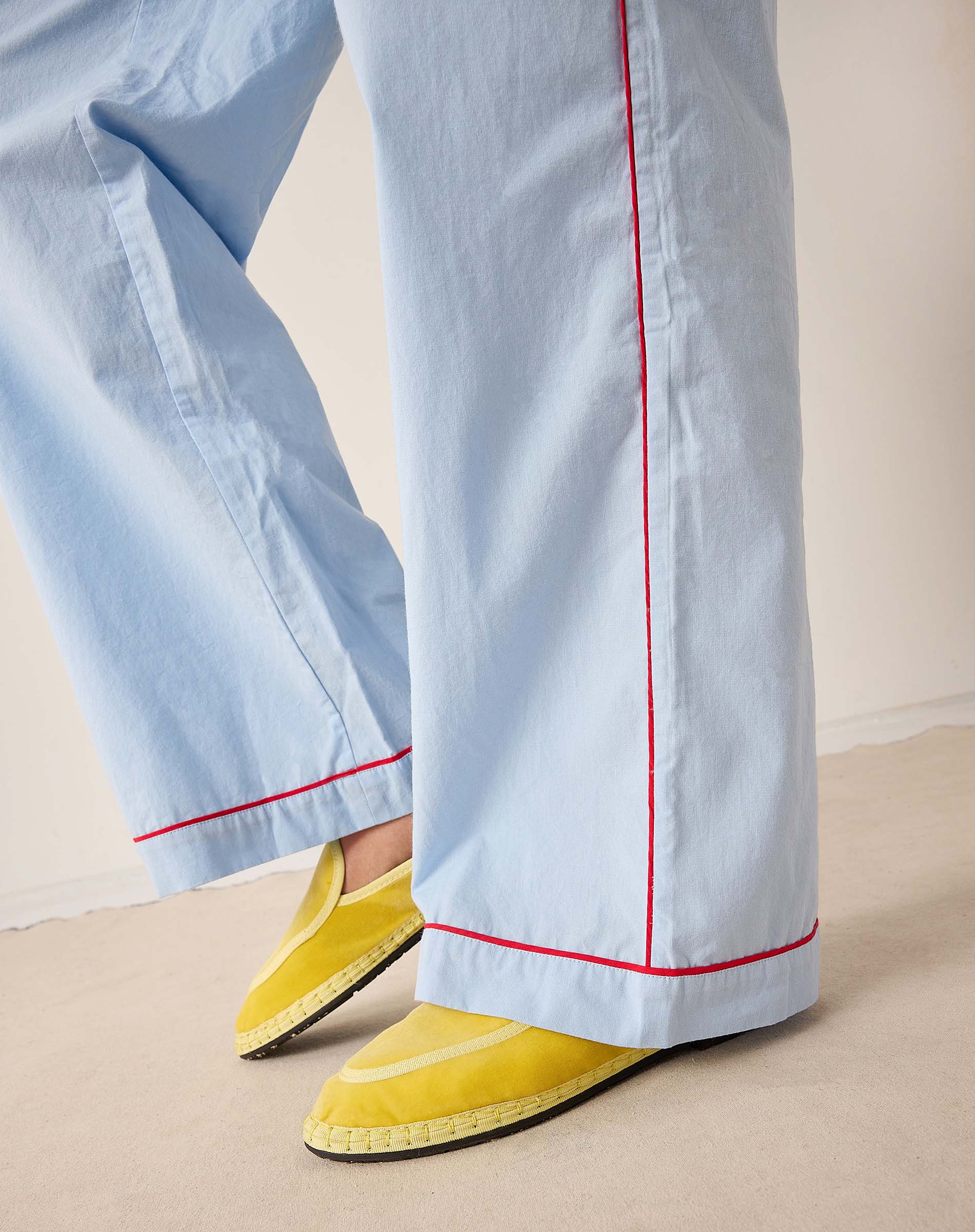Light blue pants with red piping and yellow shoes on a neutral background