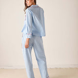 Woman wearing a light blue pajama set with red piping on a beige background