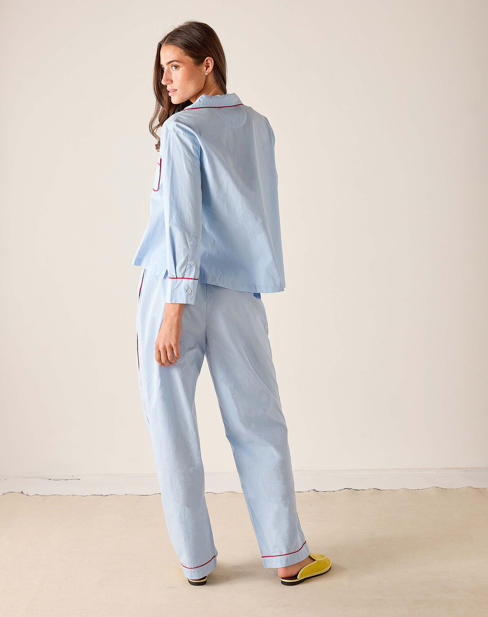 Woman wearing a light blue pajama set with red piping on a beige background