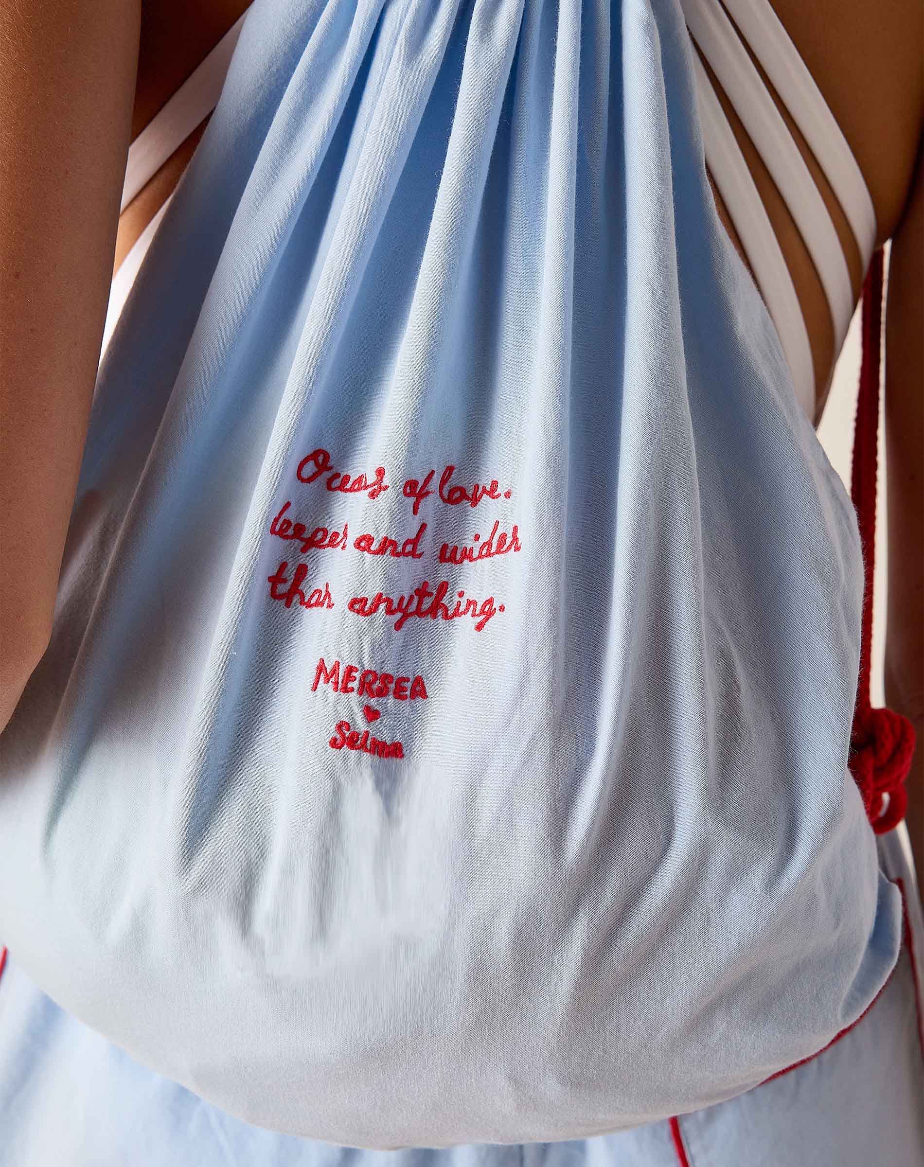 White drawstring bag with red text held by a person