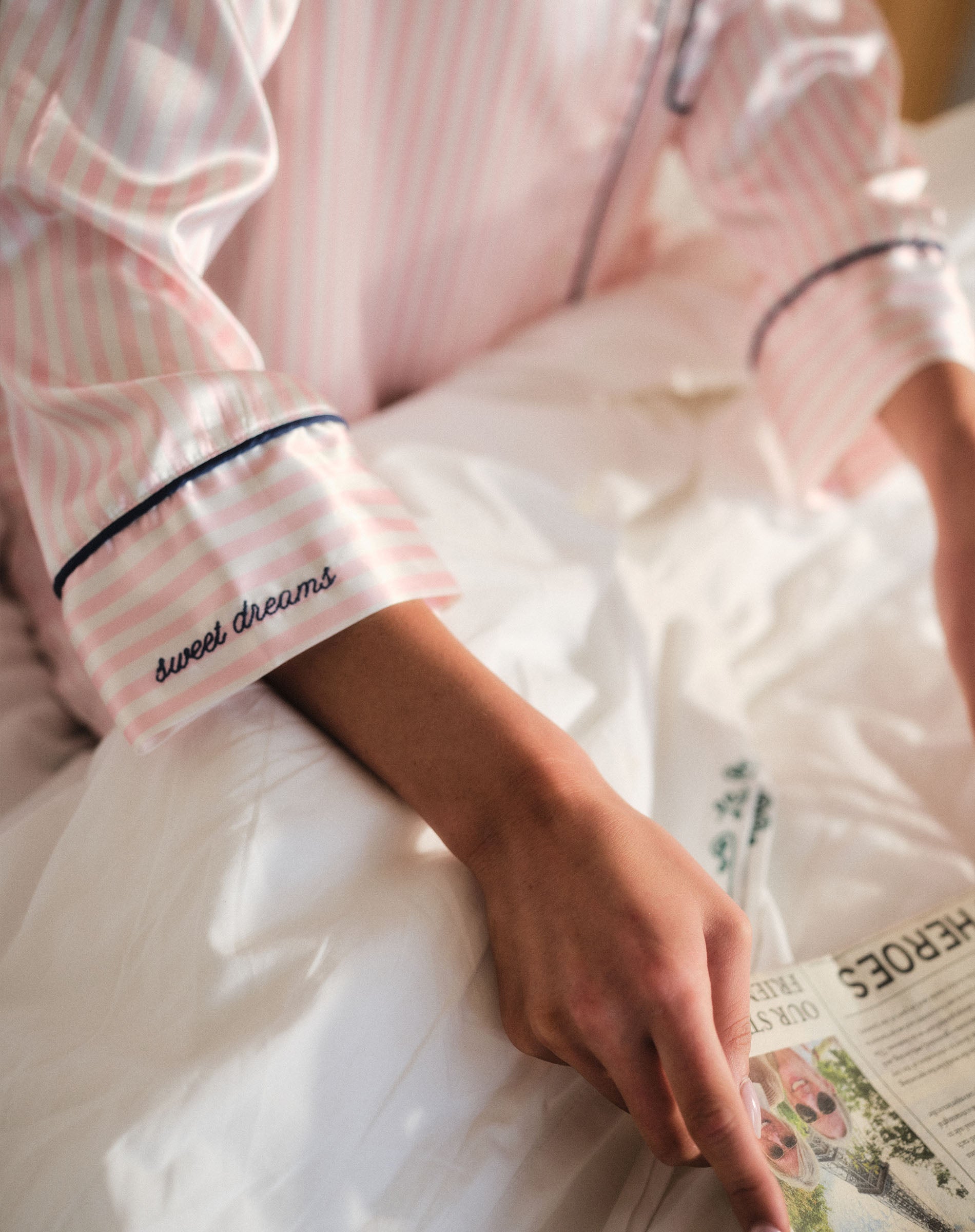 Person wearing a pink and white striped robe with 'sweet dreams' text, holding a newspaper.