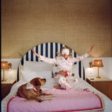 Woman in a pink robe sitting on a bed with a dog, in a bedroom setting.