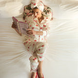 Woman in pajama set with red lip prints reading a book on a bed.