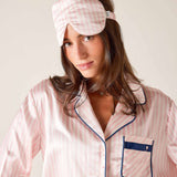 Woman wearing a pink striped pajama set and matching sleep mask.