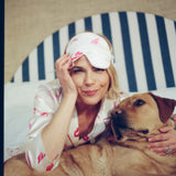 Woman in pajamas with a dog wearing a sleep mask on a striped chair.