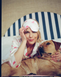 Woman in pajamas with a dog wearing a sleep mask on a striped chair.