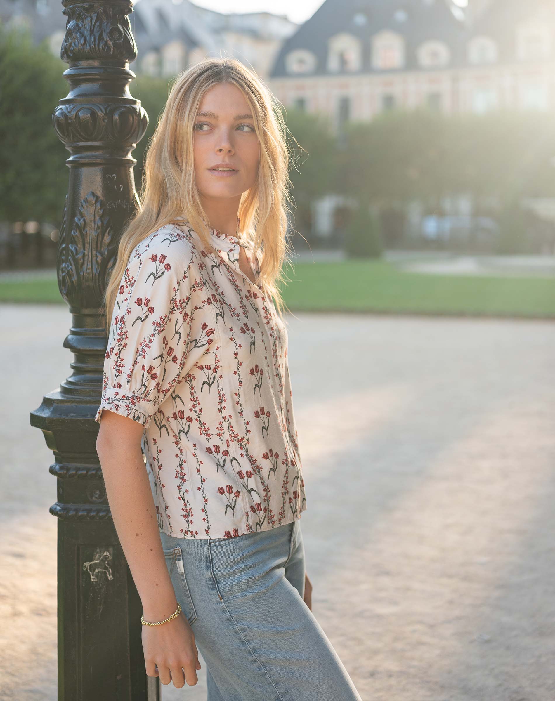 Woman wearing a short-sleeved, cream-colored shirt with a floral blossom and berry print and light-wash denim jeans.