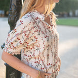 Model in a cream and orange flower market print short-sleeve blouse paired with light-wash denim jeans.