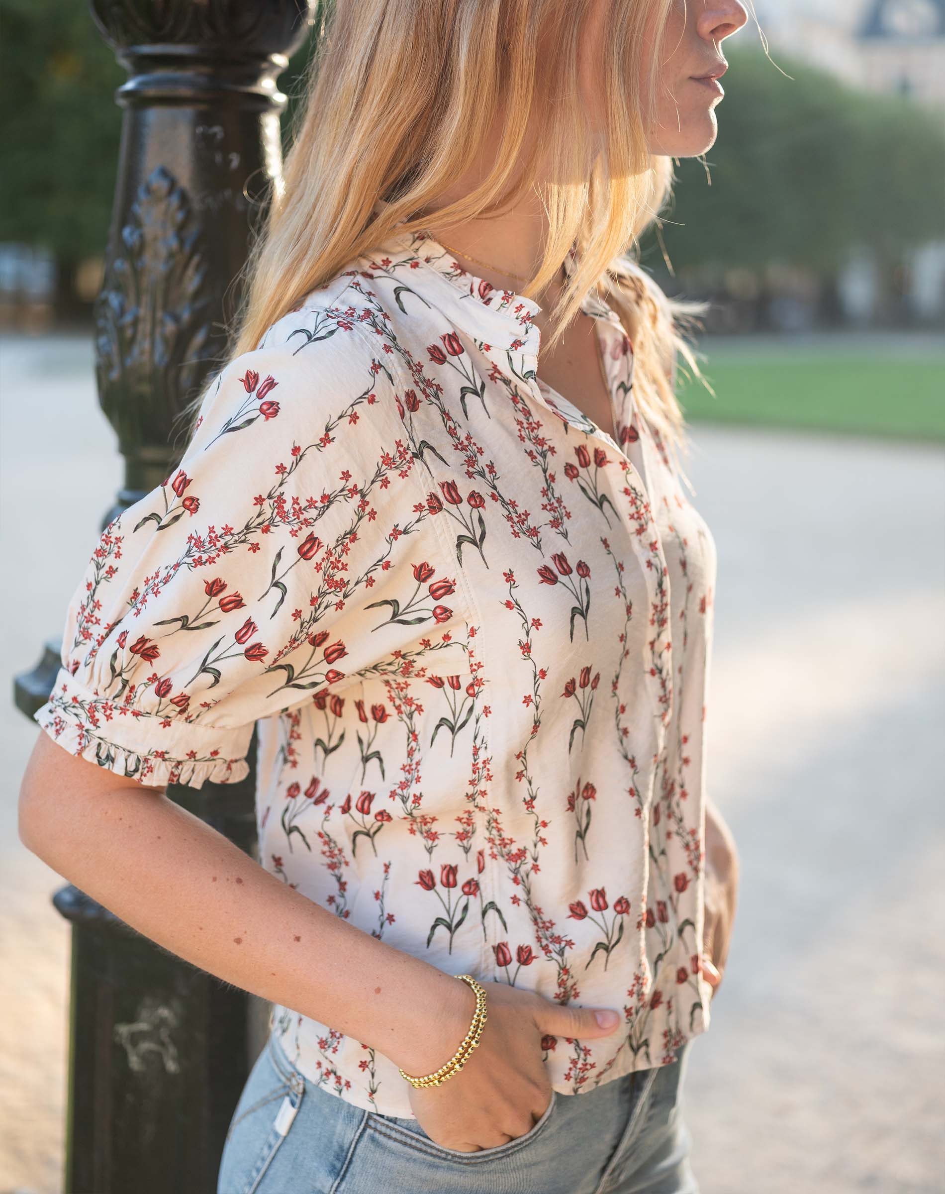Model in a cream and orange flower market print short-sleeve blouse paired with light-wash denim jeans.