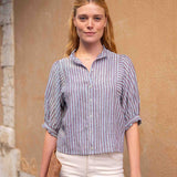 Woman wearing a striped shirt and white pants standing against a beige wall.