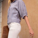 Woman wearing a striped shirt and white pants against a beige wall