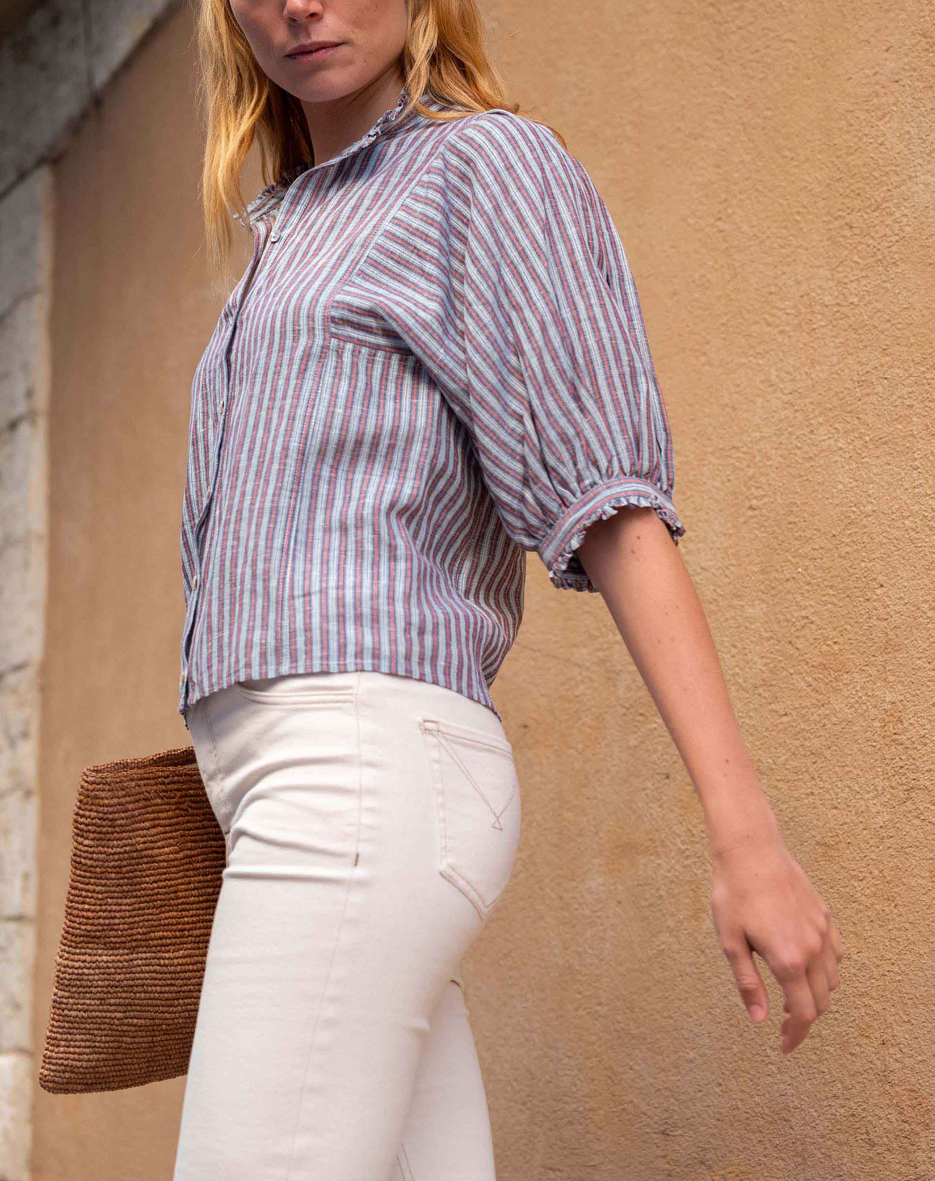 Woman wearing a striped shirt and white pants against a beige wall