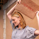 Woman holding a doormat with 'NEREA' branding outdoors.