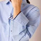 Ladies' travel-ready oxford blue button-down shirt with a slim fit and cotton fabric featuring decorative navy trim on the cuff.