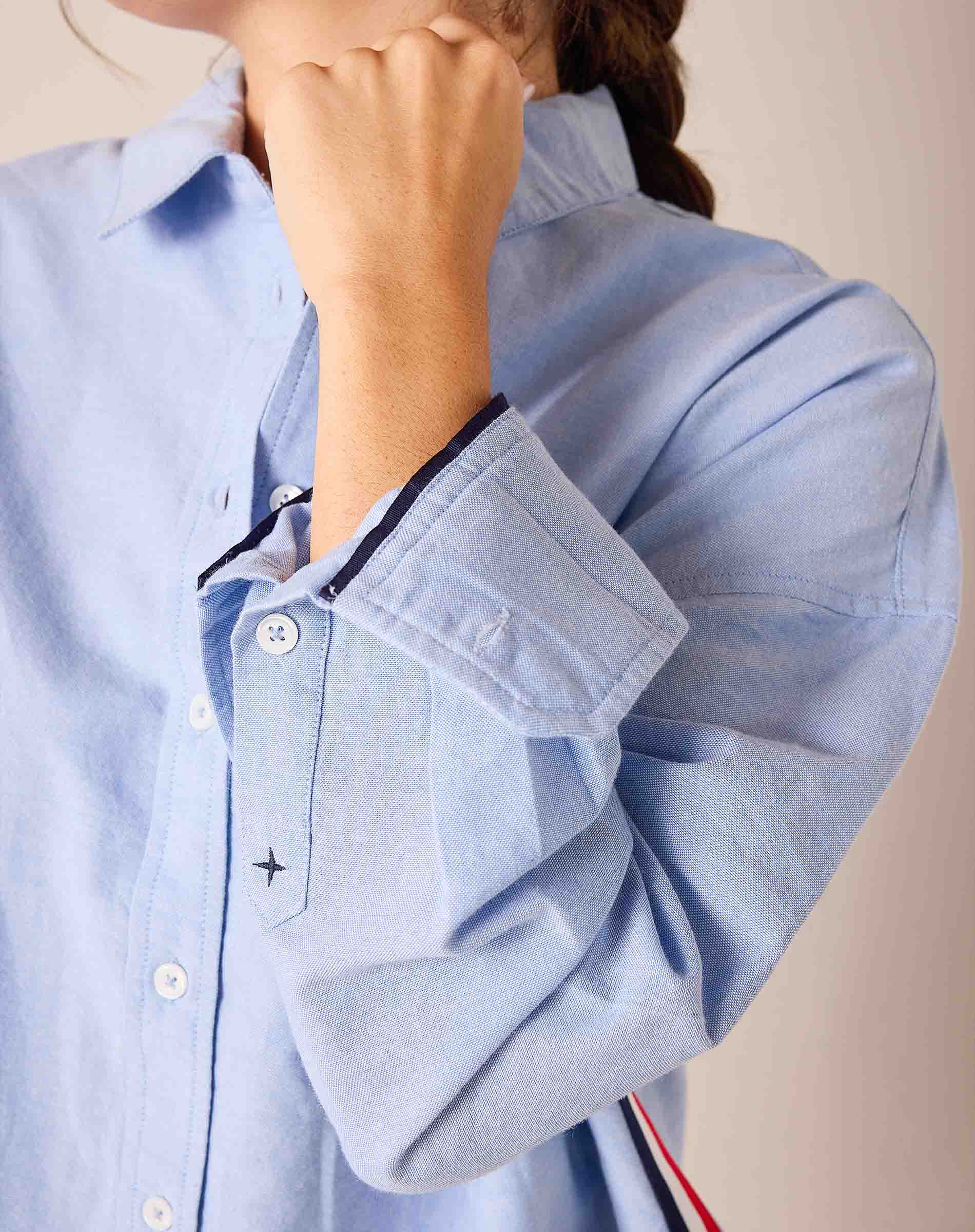 Ladies' travel-ready oxford blue button-down shirt with a slim fit and cotton fabric featuring decorative navy trim on the cuff.