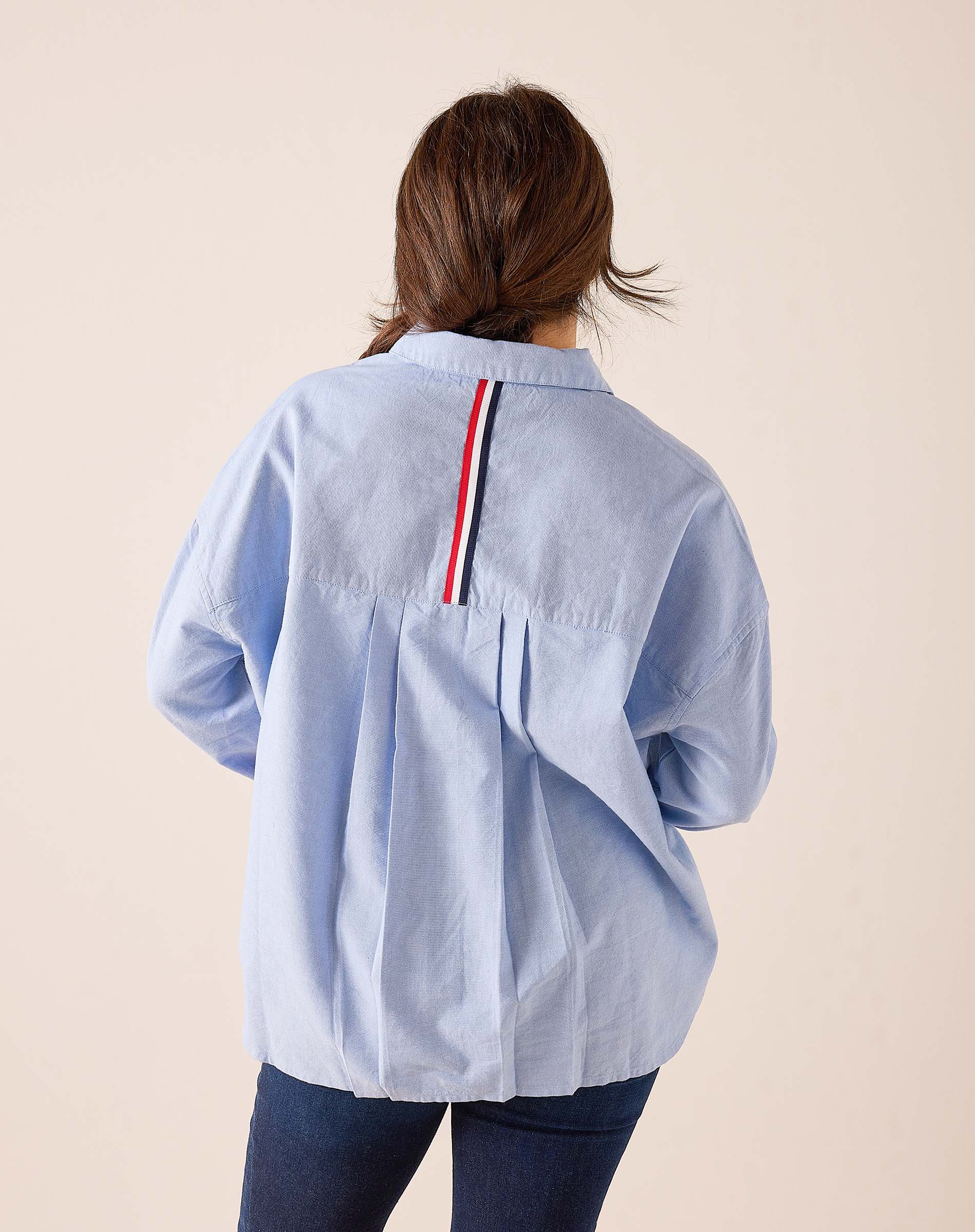 Back view of women's travel-friendly Oxford blue button-down shirt featuring a striped detail on the back yoke.