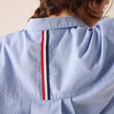 Back view of the Oxford blue cotton blend shirt featuring a vertical red, white, and navy striped detail on the back yoke.