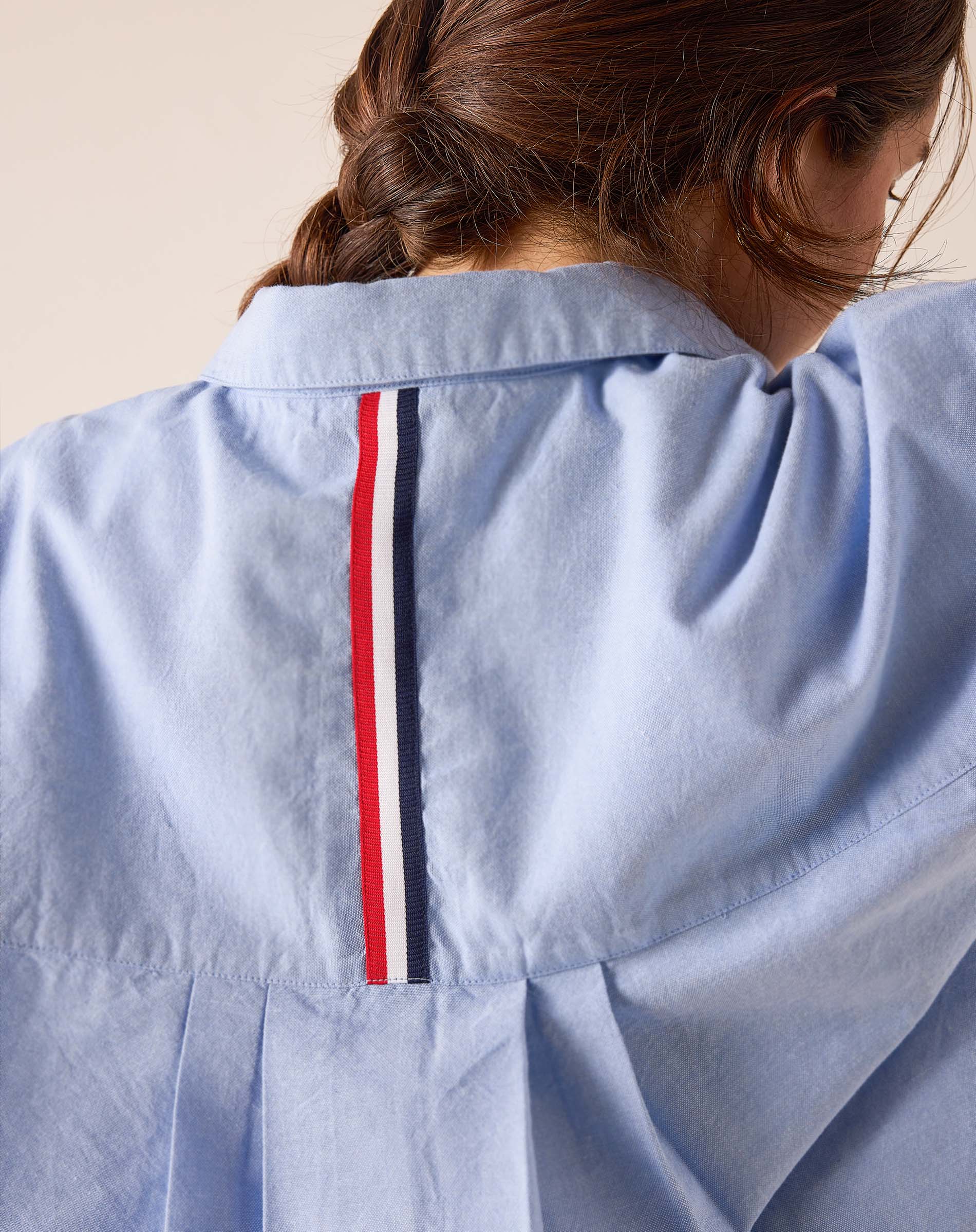 Back view of the Oxford blue cotton blend shirt featuring a vertical red, white, and navy striped detail on the back yoke.