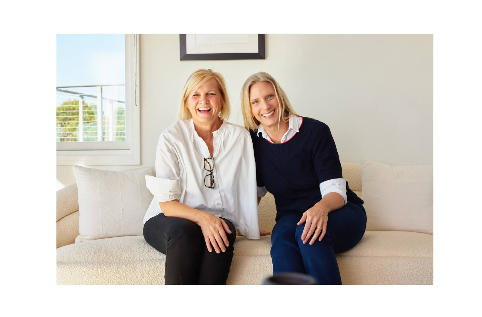 Mersea Founders Melanie Bolin and Lina Dickinson Sitting Side by Side on White Couch with White Background