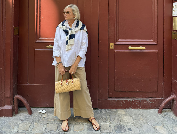 Woman standing in front of a red door wearing a white shirt, beige pants, and a striped scarf.