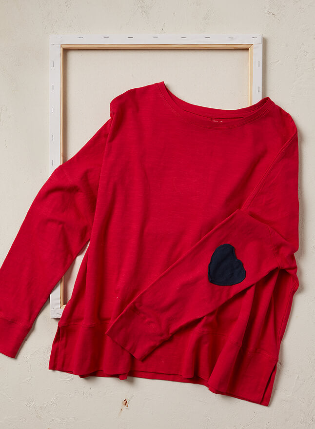 Red long-sleeve shirt with a black heart design on a beige background