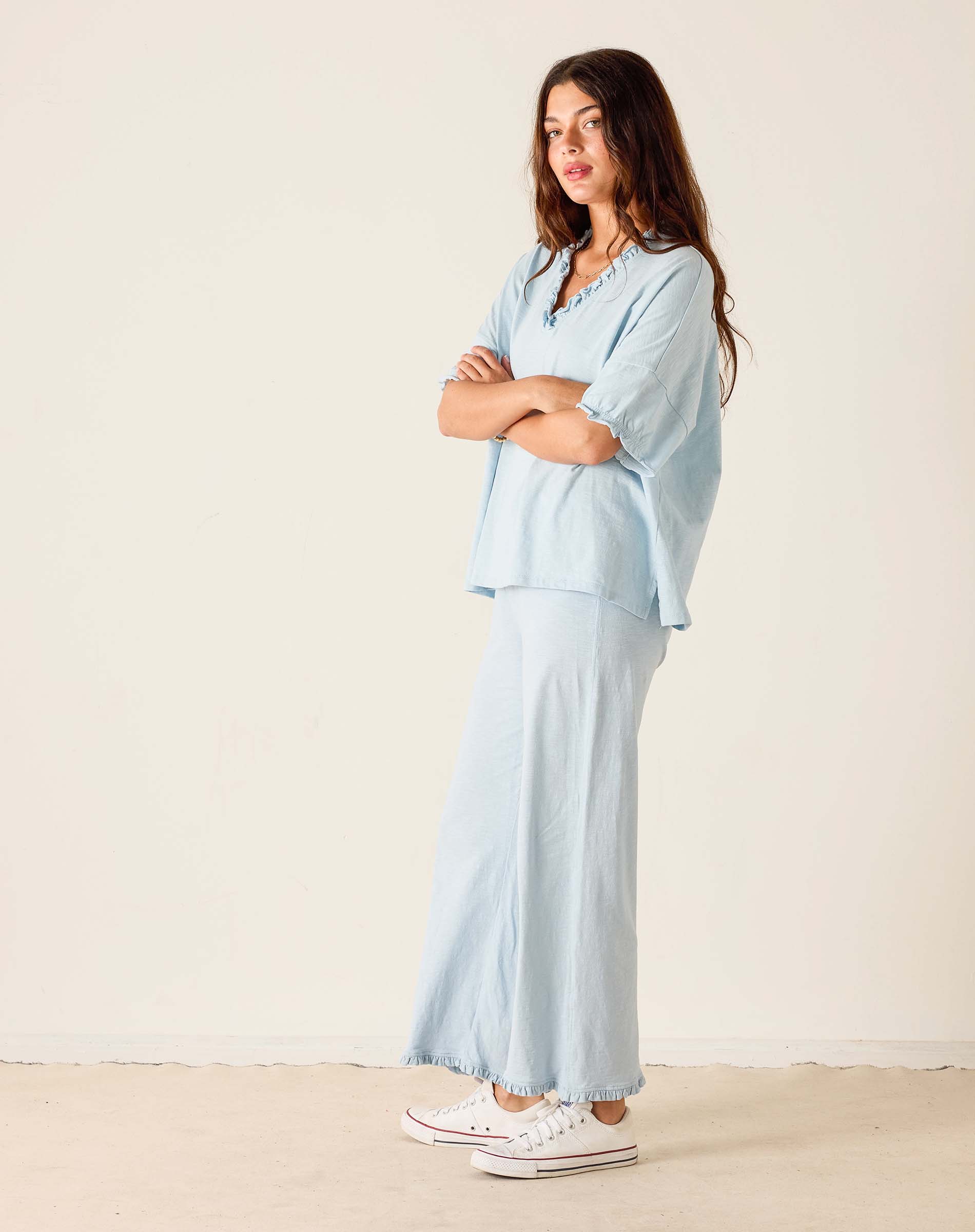 Woman wearing a light blue outfit with white sneakers on a beige background
