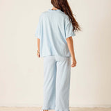 Woman wearing a light blue outfit with wide-leg pants against a plain background