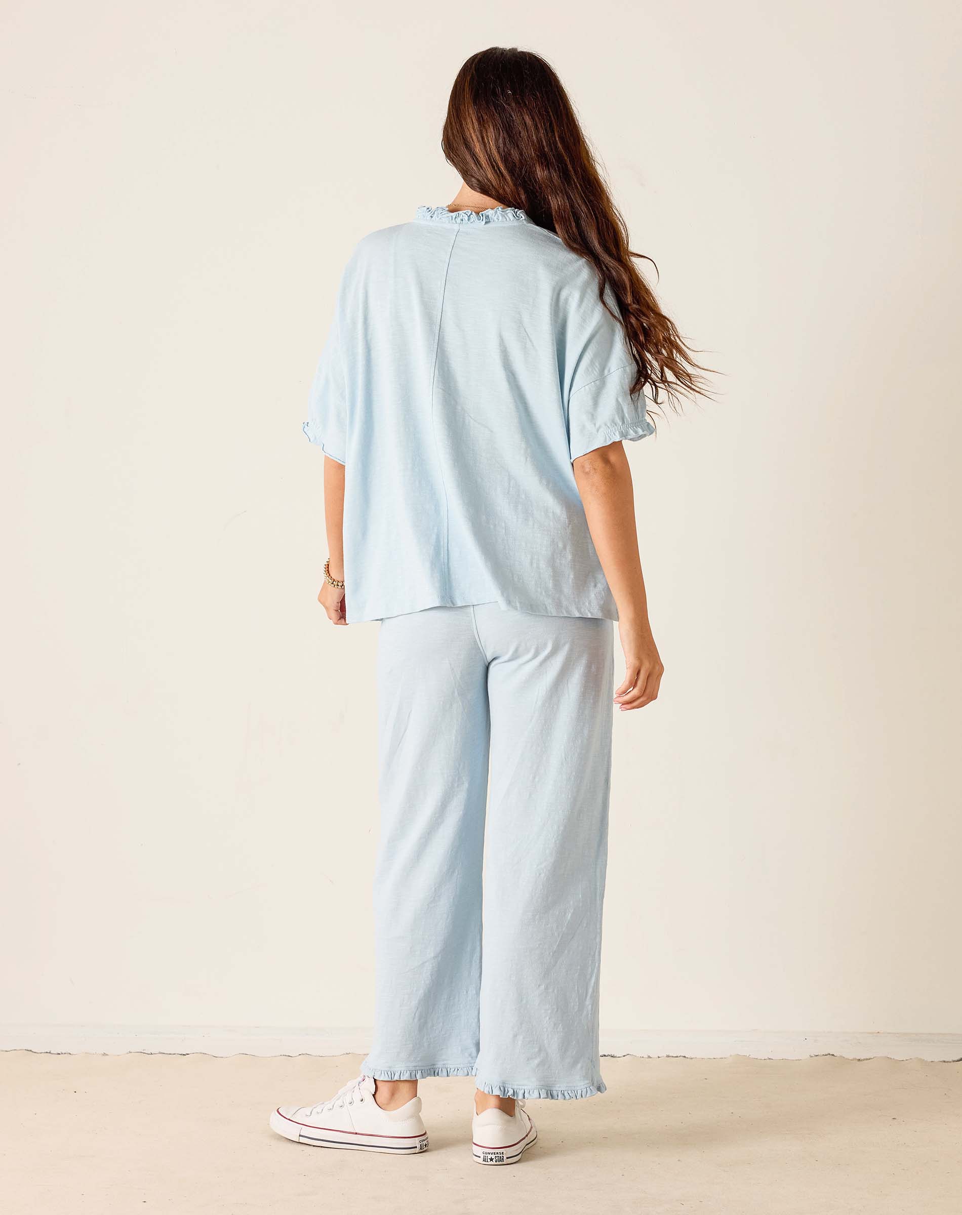 Woman wearing a light blue outfit with wide-leg pants against a plain background