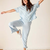 Woman in light blue outfit posing with arms outstretched on a plain background