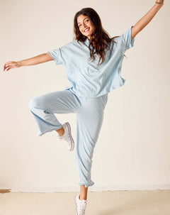 Woman in light blue outfit posing with arms outstretched on a plain background
