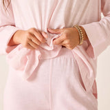 Person wearing a light pink outfit with a close-up of hands adjusting the fabric.