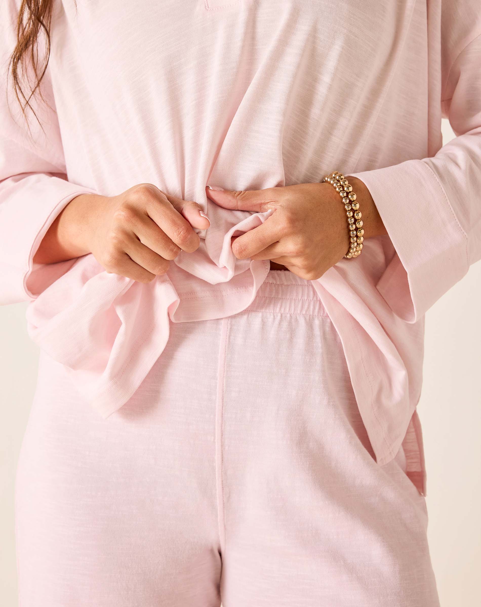Person wearing a light pink outfit with a close-up of hands adjusting the fabric.