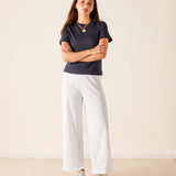 Woman wearing a navy t-shirt and white pants standing against a plain background
