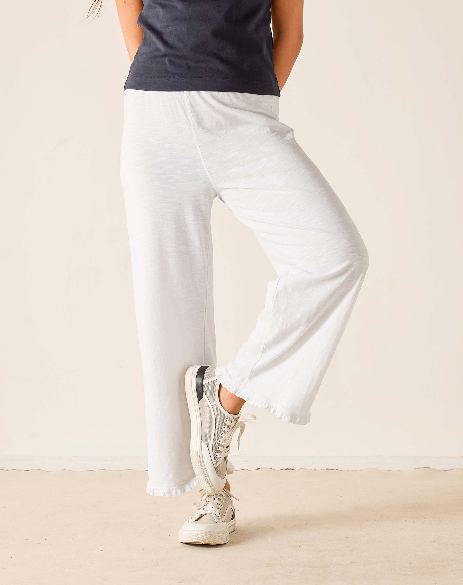 Person wearing white pants and white sneakers on a plain background