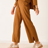 Person wearing a brown outfit with wide-leg pants and beige sneakers on a white background