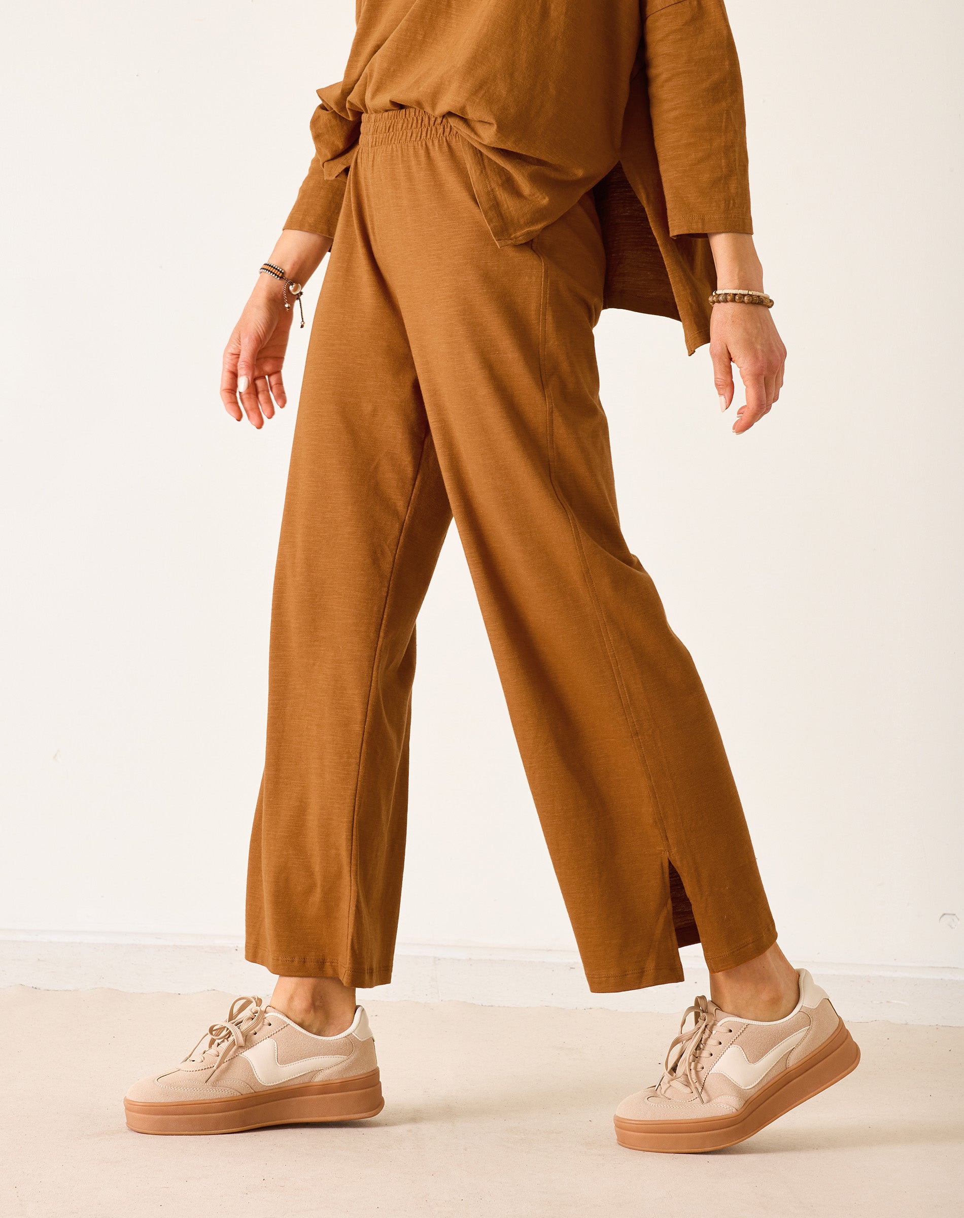 Person wearing a brown outfit with wide-leg pants and beige sneakers on a white background