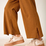Person wearing brown pants and beige sneakers on a neutral background