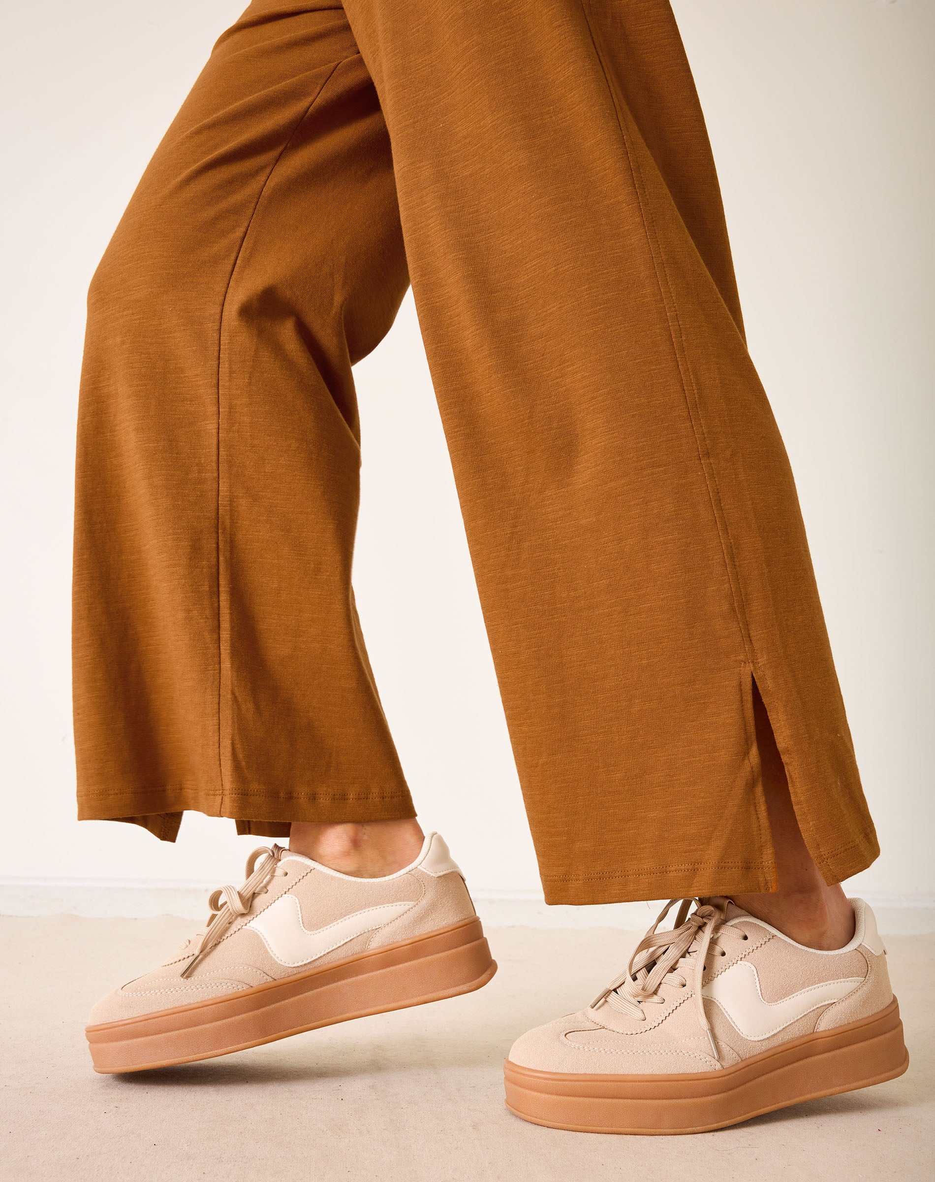 Person wearing brown pants and beige sneakers on a neutral background