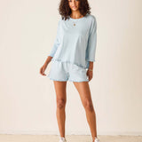 Woman wearing a light blue outfit with shorts and a top, standing against a plain background.